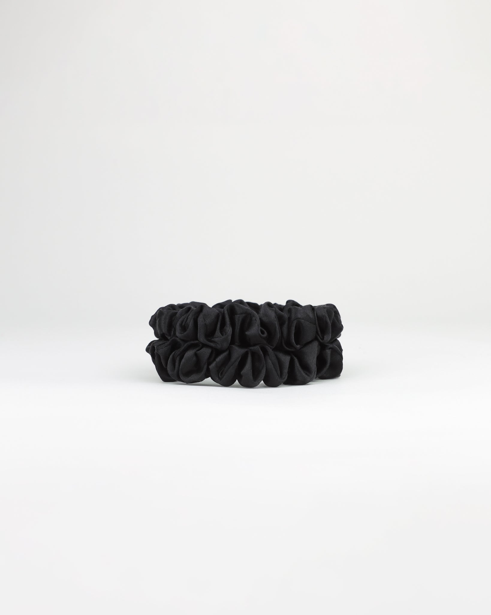 Two medium sized black scrunchies on a white background