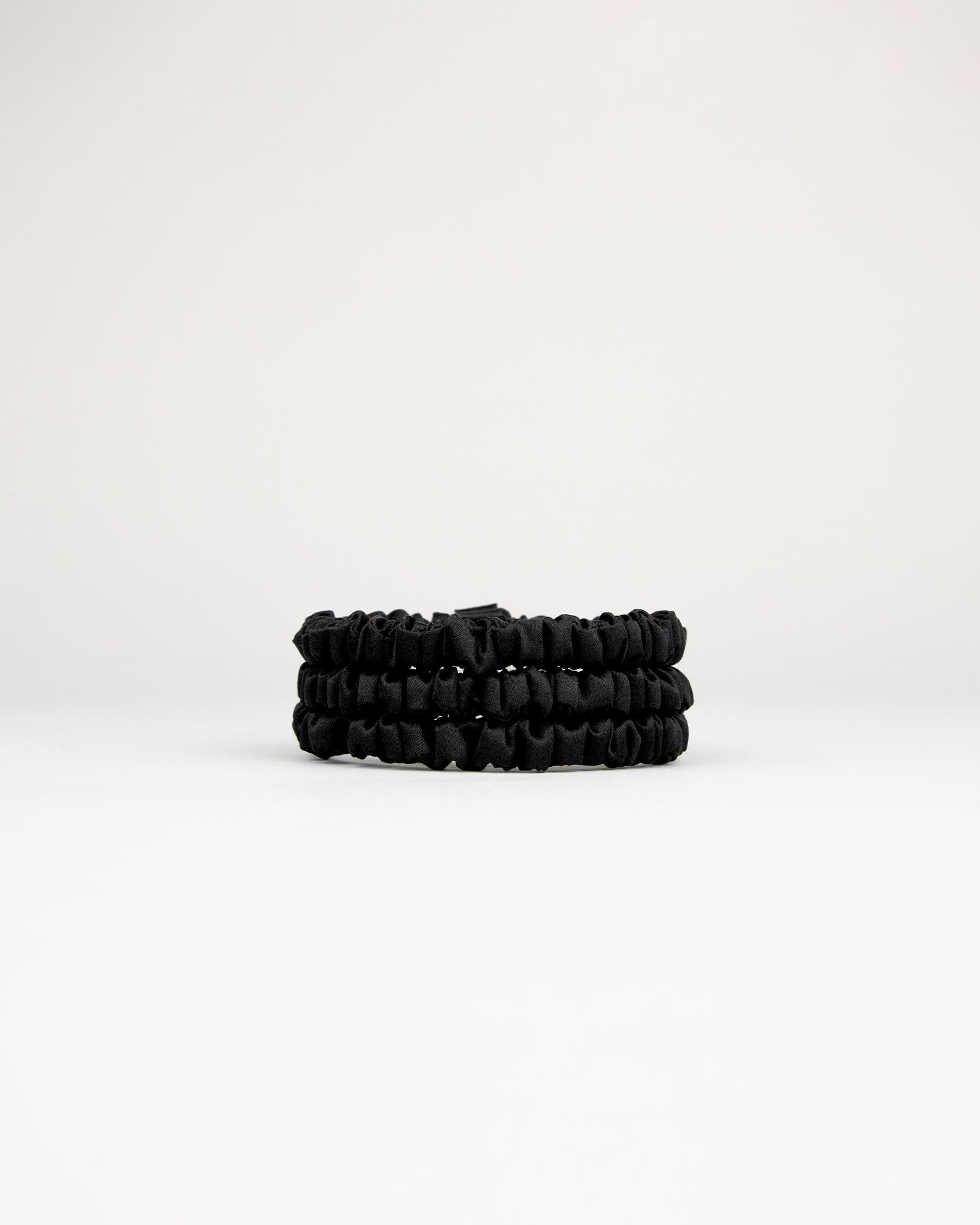 Set of three black silk scrunchies stacked on a white background